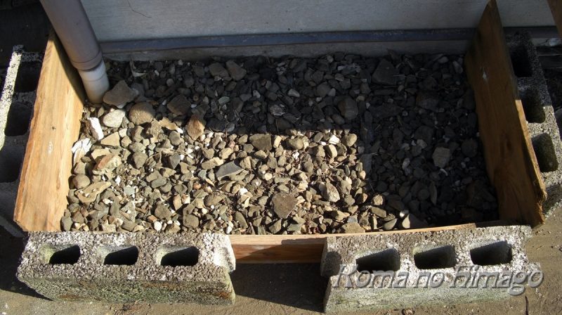板とブロックで月った植えつけ場所に小石を敷く